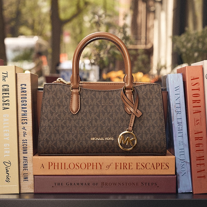 bolso de mano de piel en tono marr&oacute;n sobre una pila de libros