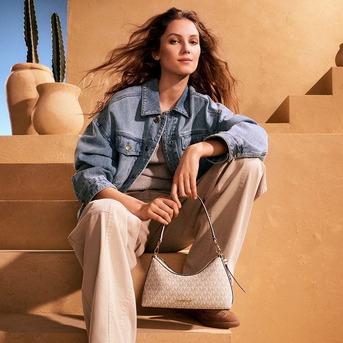 modelo con chaqueta de denim y bolso de mano de piel en tono crema con logotipo
