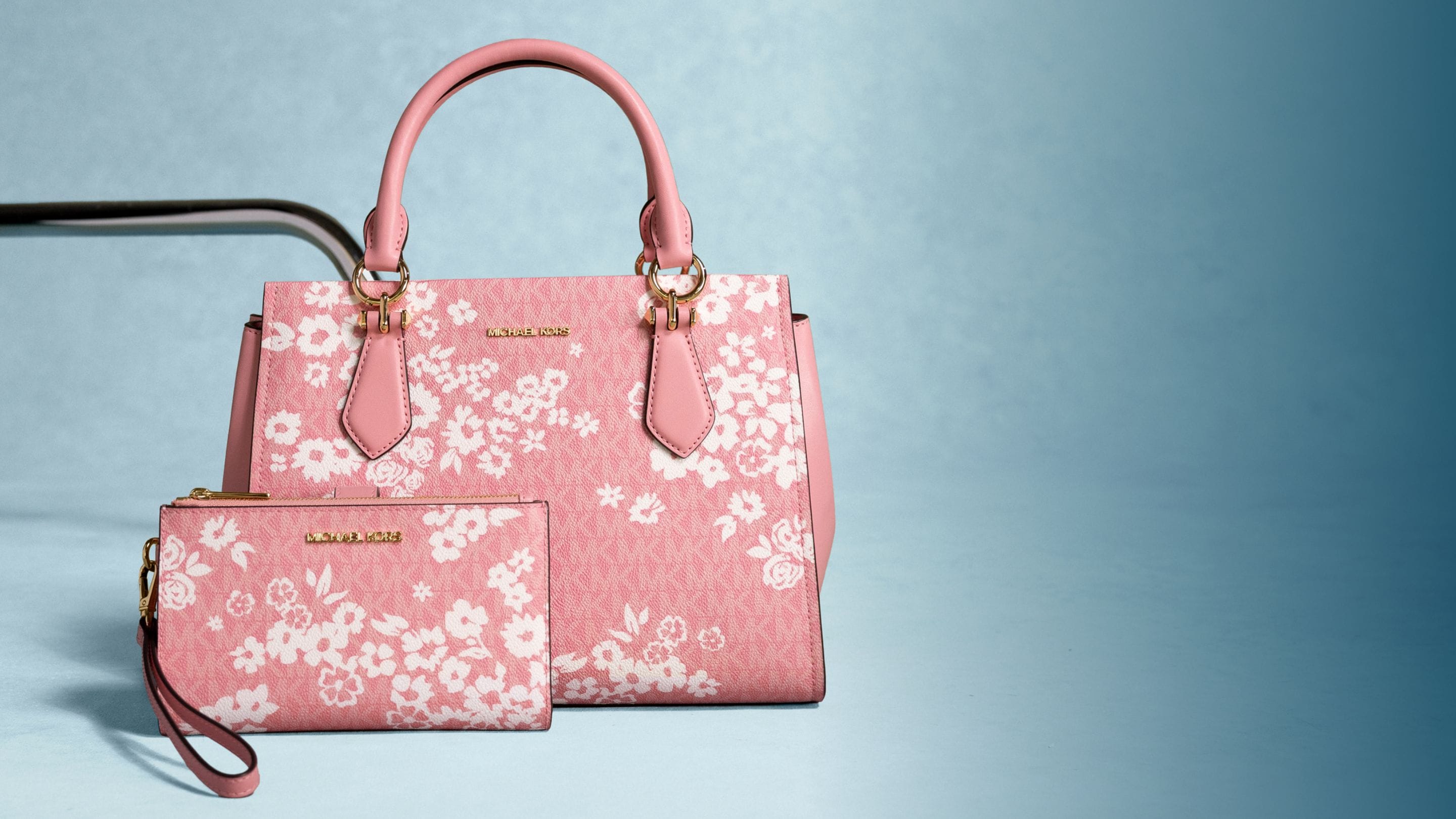 pink handbag and wallet with white floral pattern on blue background