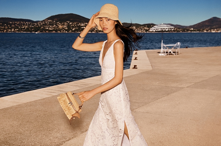 model wearing white dress, straw bucket hat and crochet crossbody bag